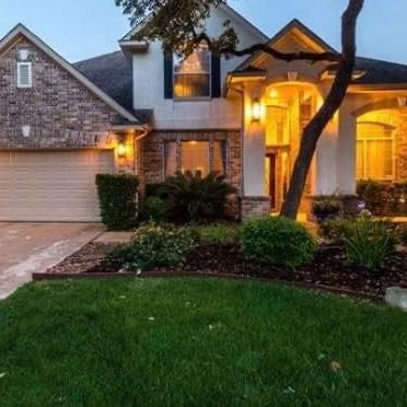 Nicely landscaped front yard of home with lights on.